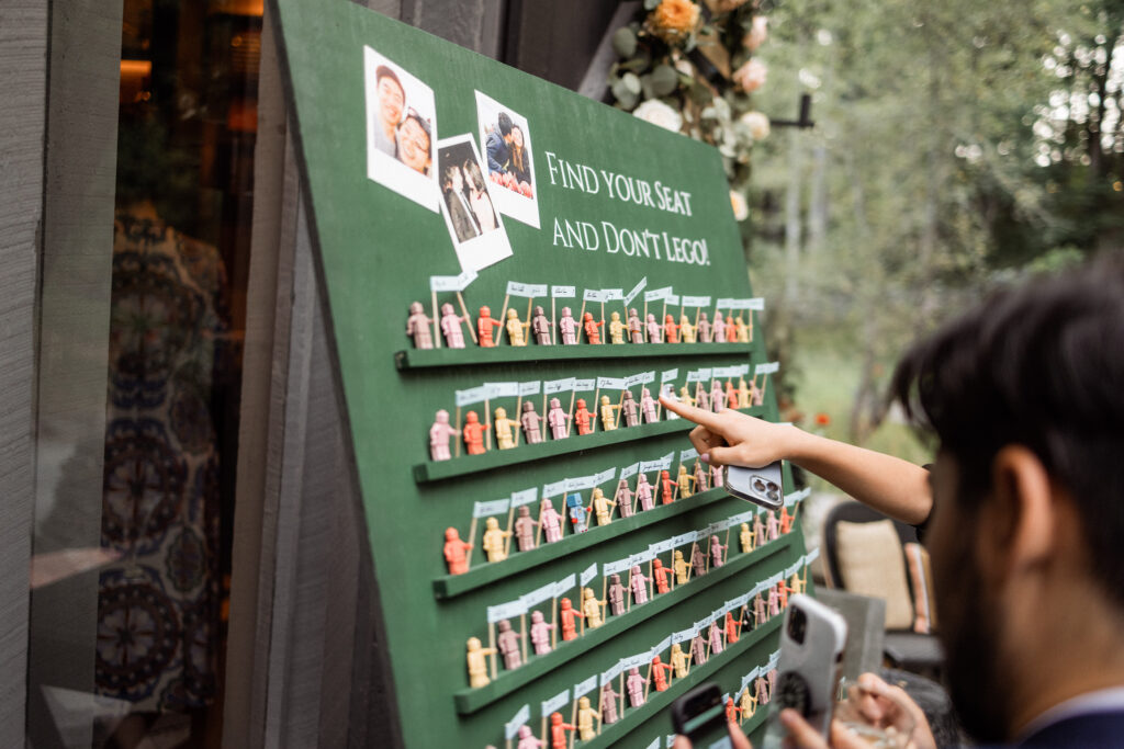 Wedding guests find their seats at a display full of legos. The seating chart says, "Find your seat and don't 'Lego'."