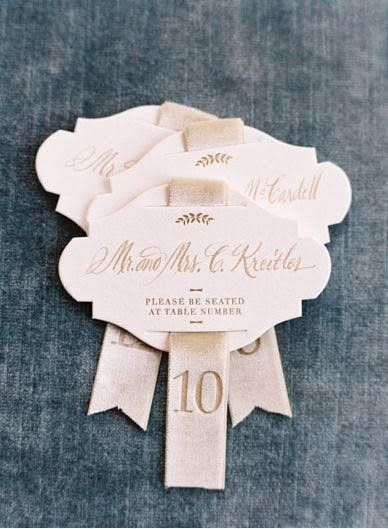 A set of luxurious wedding escort cards double as place cards. They are dies cut in a sophisticated crenelle shape with high-quality ivory paper, elegant calligraphy, and velvet ribbon, and feature monograms and classic fonts, perfect for setting the tone of an old money wedding.