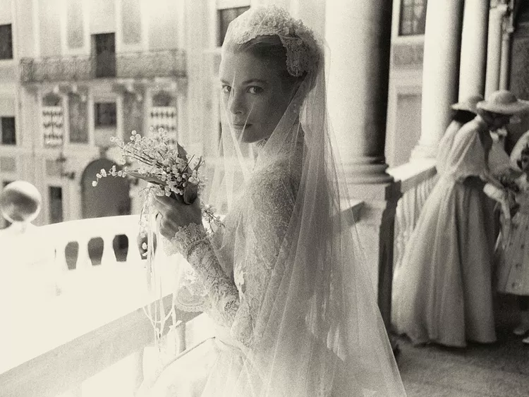 Grace Kelly standing elegantly in her wedding gown, marrying the Prince of Monaco in 1956. Her timeless style embodies the old money wedding aesthetic with a classic lace gown and a serene, poised demeanor.