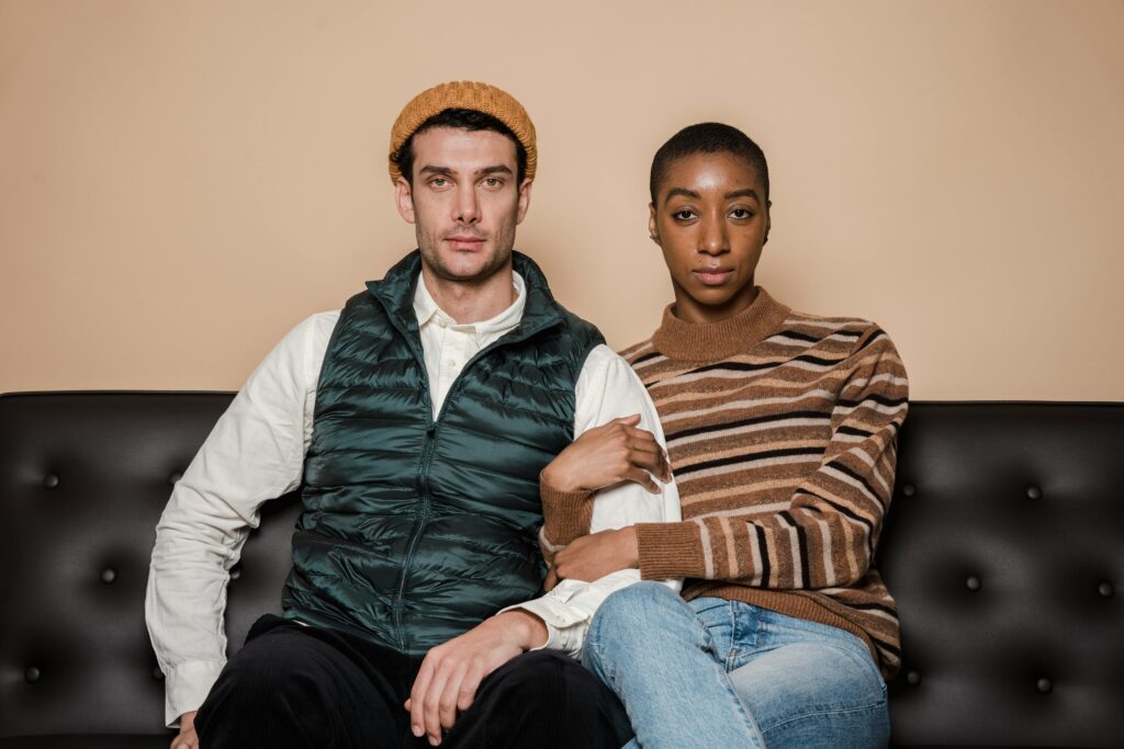 A smug couple sitting arm-in-arm on a black leather couch.