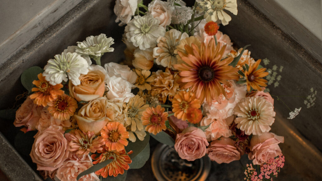 Close-up of lush floral arrangements in a mix of orange, peach, coral, and cream blooms, artfully arranged for a romantic, nature-inspired wedding