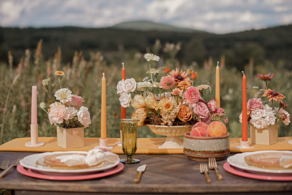 Rustic outdoor wedding table setting with a vibrant centerpiece of pink and orange flowers, set against the backdrop of the Catskill mountains