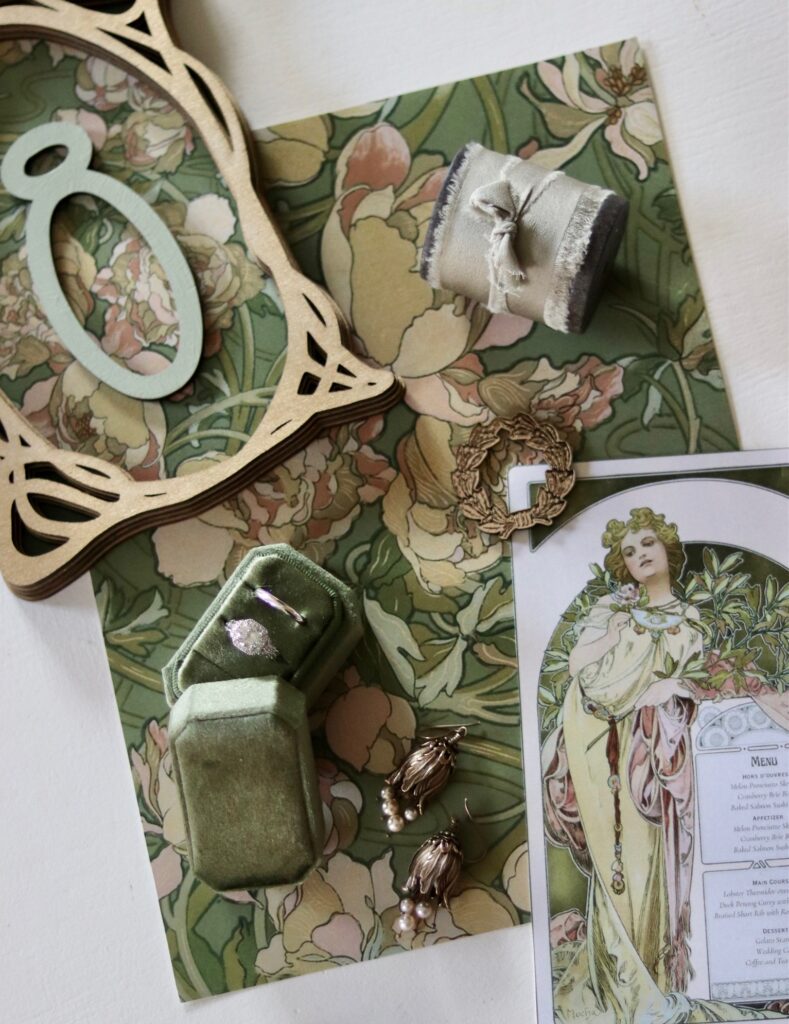 Flatlay of Art Nouveau-inspired wedding details with vintage rings, floral motif paper goods, and soft velvet textures by Idyllwild Event Design