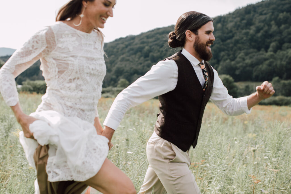 Bride and groom walking through tall grass at golden hour, with warm-toned wildflowers and a gentle breeze in the Catskills