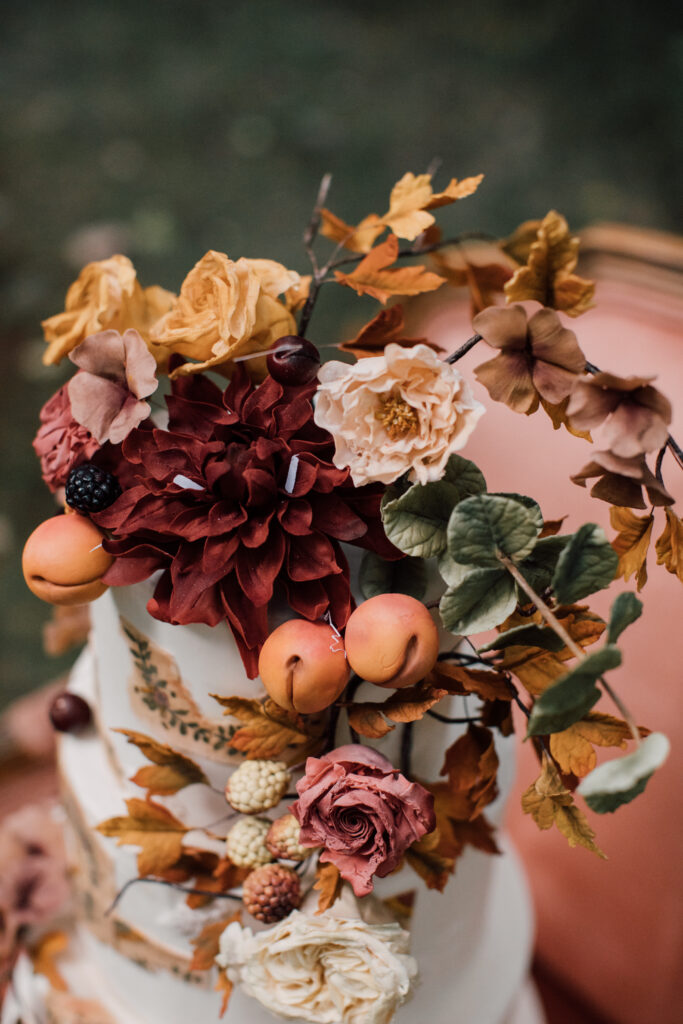 Detail of an elegant wedding cake with autumn flowers and fruit, hand-painted sugar details, and a painterly finish by Mamie Brougitte Cakes