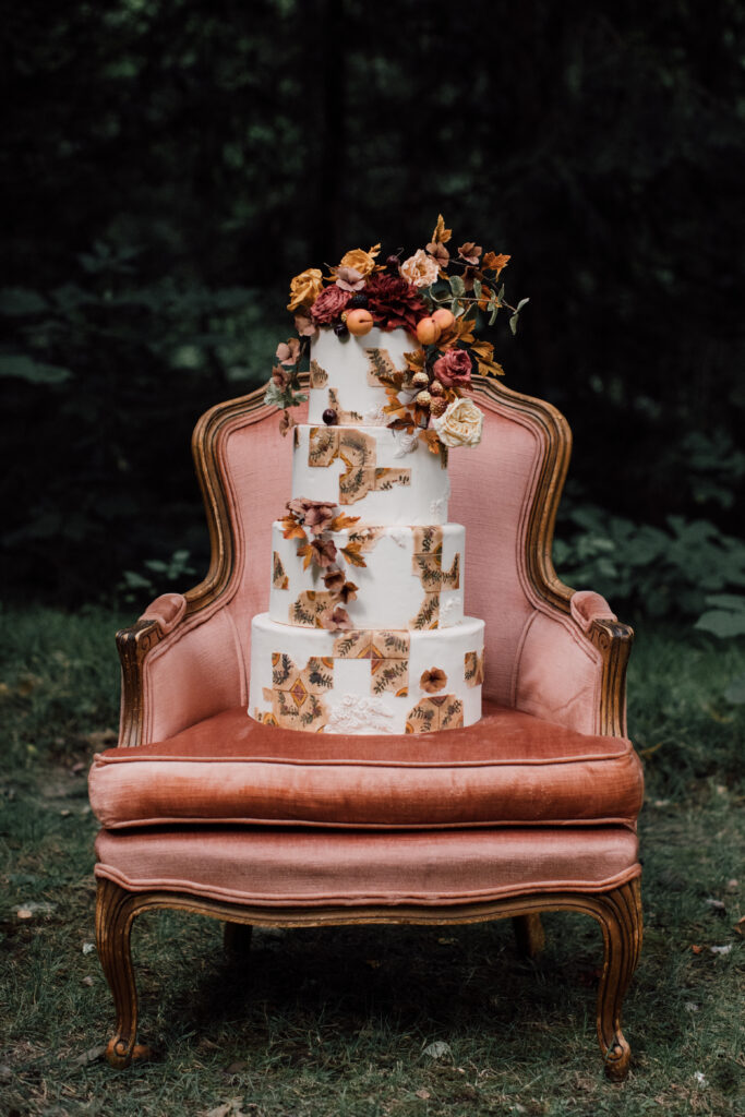 A bohemian peach and gold wedding cake sitting on a rose velvet armchair