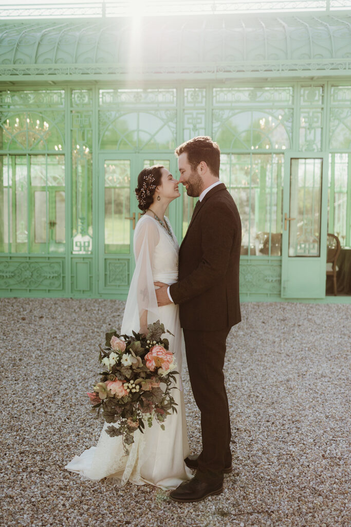 Bride and groom embrace in front of L’Orangerie’s glass exterior at an Art Nouveau wedding in the Hudson Valley