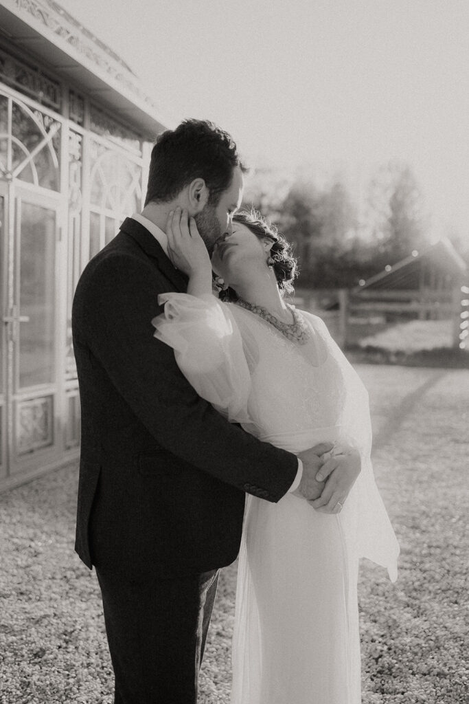 A black and white image of a bride and groom kissing outside a Victorian Greenhouse in Greenville, NY