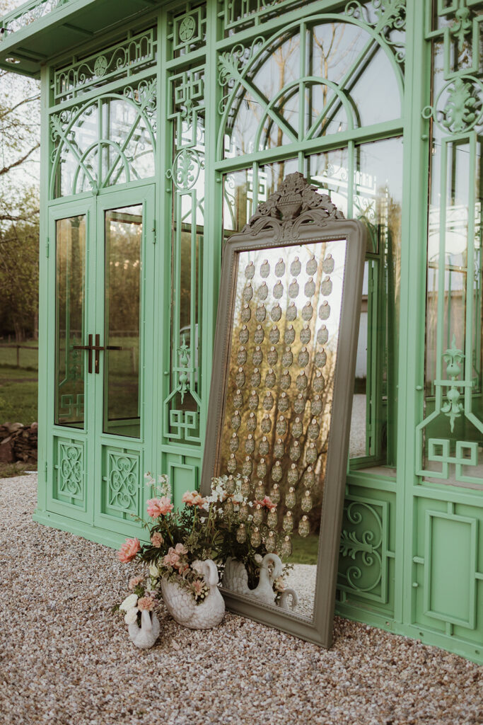 European-inspired wedding escort card display on a vintage mirror, accented with wax seals and cement swans.