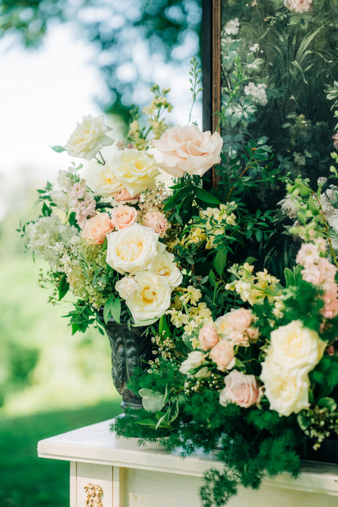 Painterly floral arrangement in cream, blush, and sage tones against architectural stone
