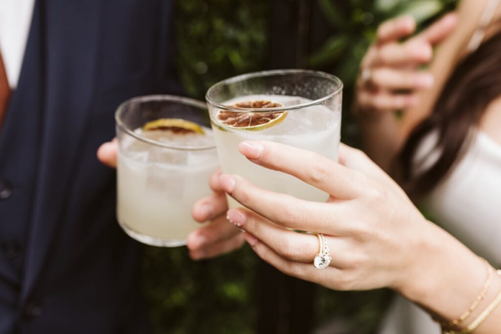 a couple clinking wedding cocktail glasses with dried citrus garnish